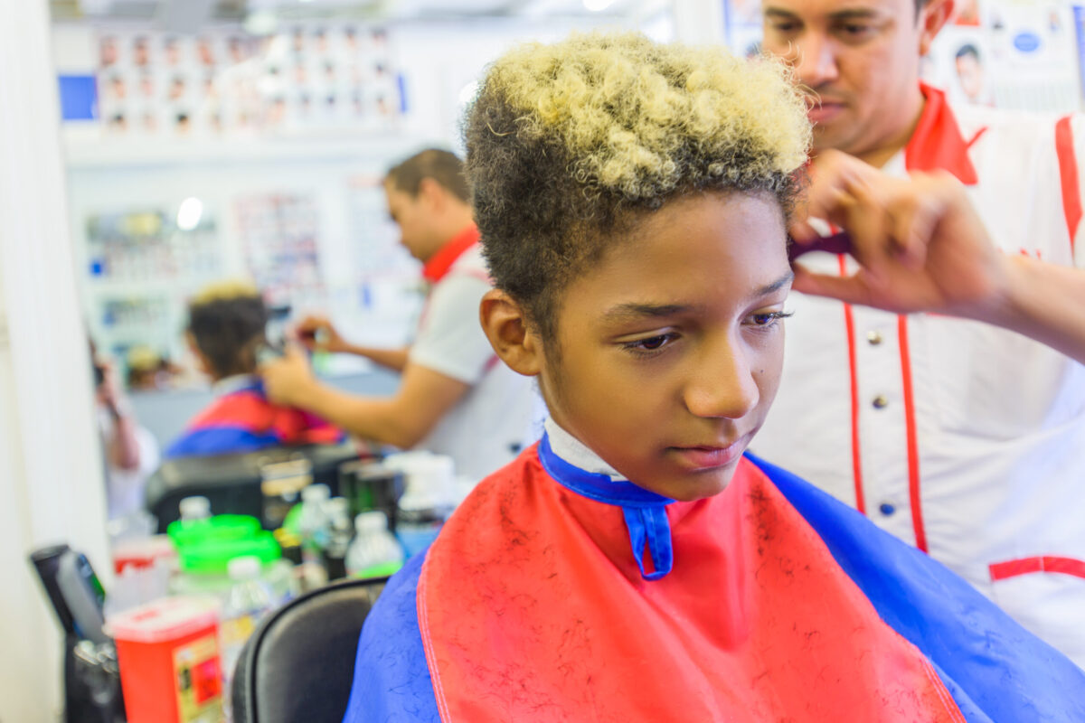 Hairdresser cutting teenage boy's hair in barbershop